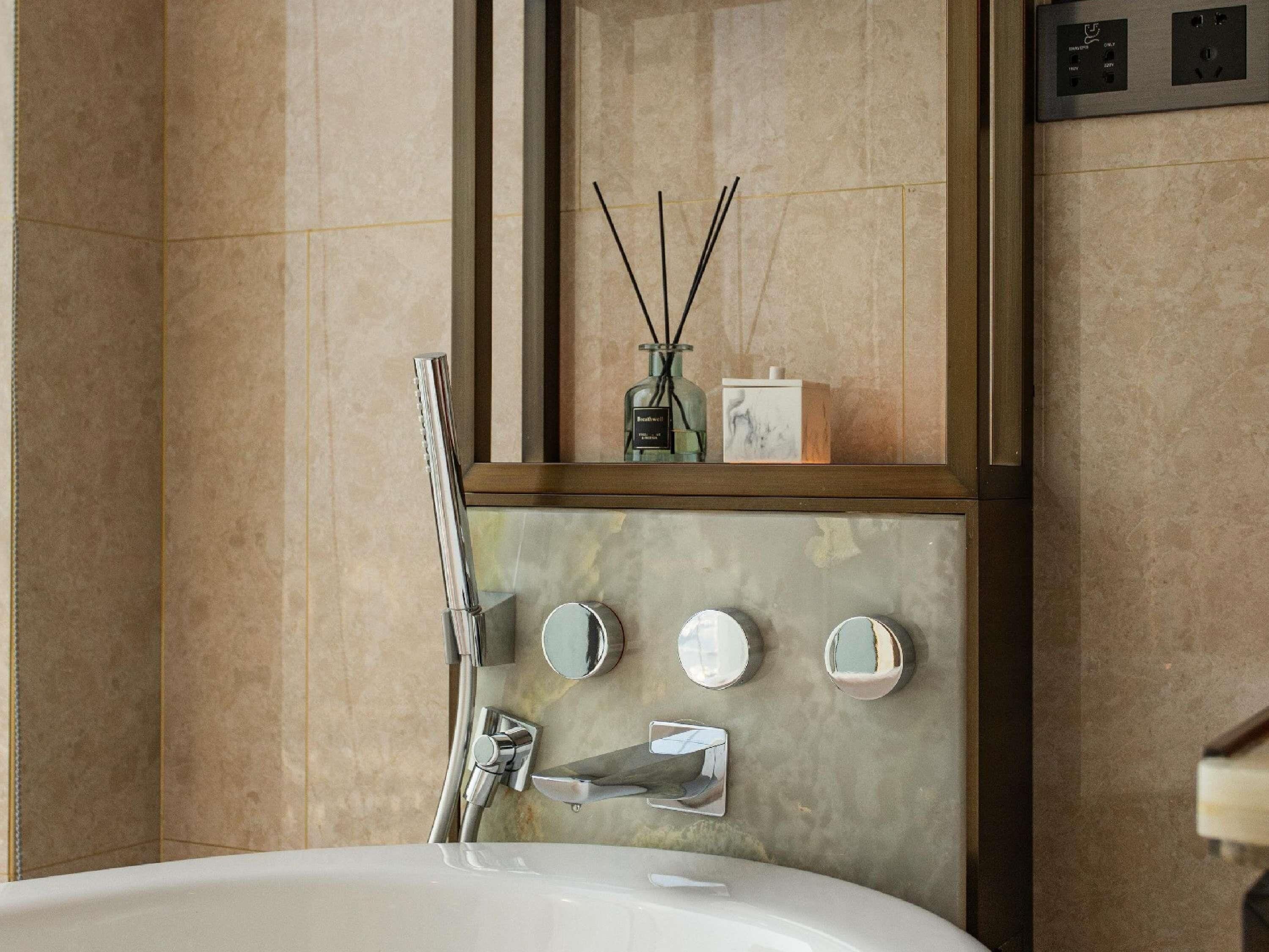 Un baño moderno con una bañera grande, un espejo montado en la pared y un florero de vidrio decorativo con ramas de juncos.