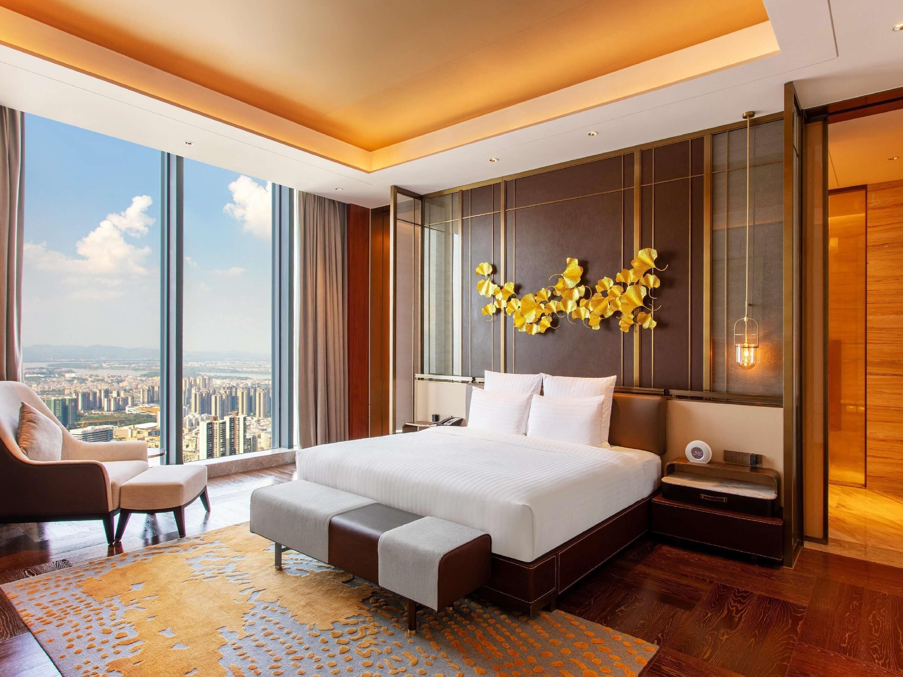 A modern hotel room with a large bed, a seating area, and a city view.