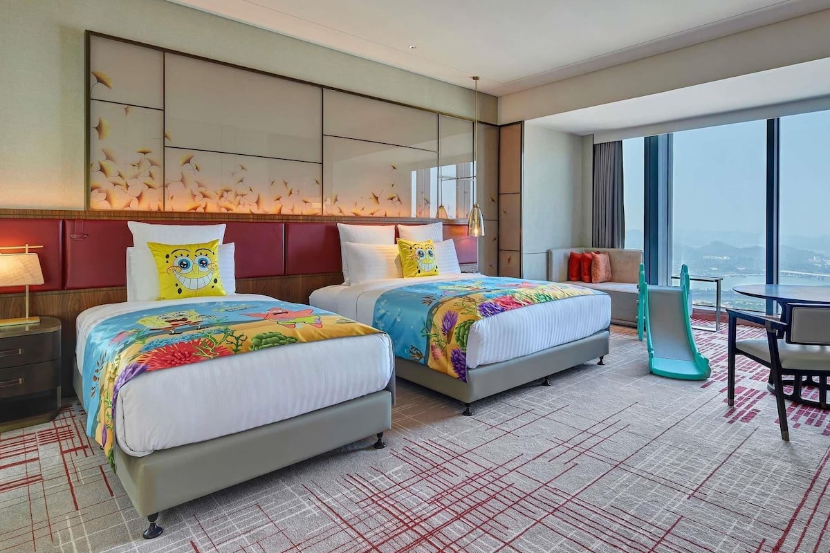Een hotelkamer met twee bedden, een groot raam met uitzicht op de stad, een zithoek en een modern design.
