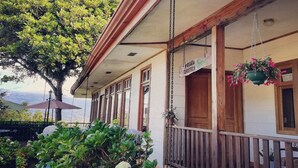 A building with a covered porch, wooden railings, and hanging flower baskets. - Best immersion experience in a Farm at Finca Queveri (Orosi)