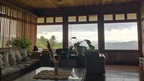 A cozy living room with a wooden ceiling, large windows, a sofa, and a coffee table with a vase of dried plants. - Best immersion experience in a Farm at Finca Queveri (Orosi)