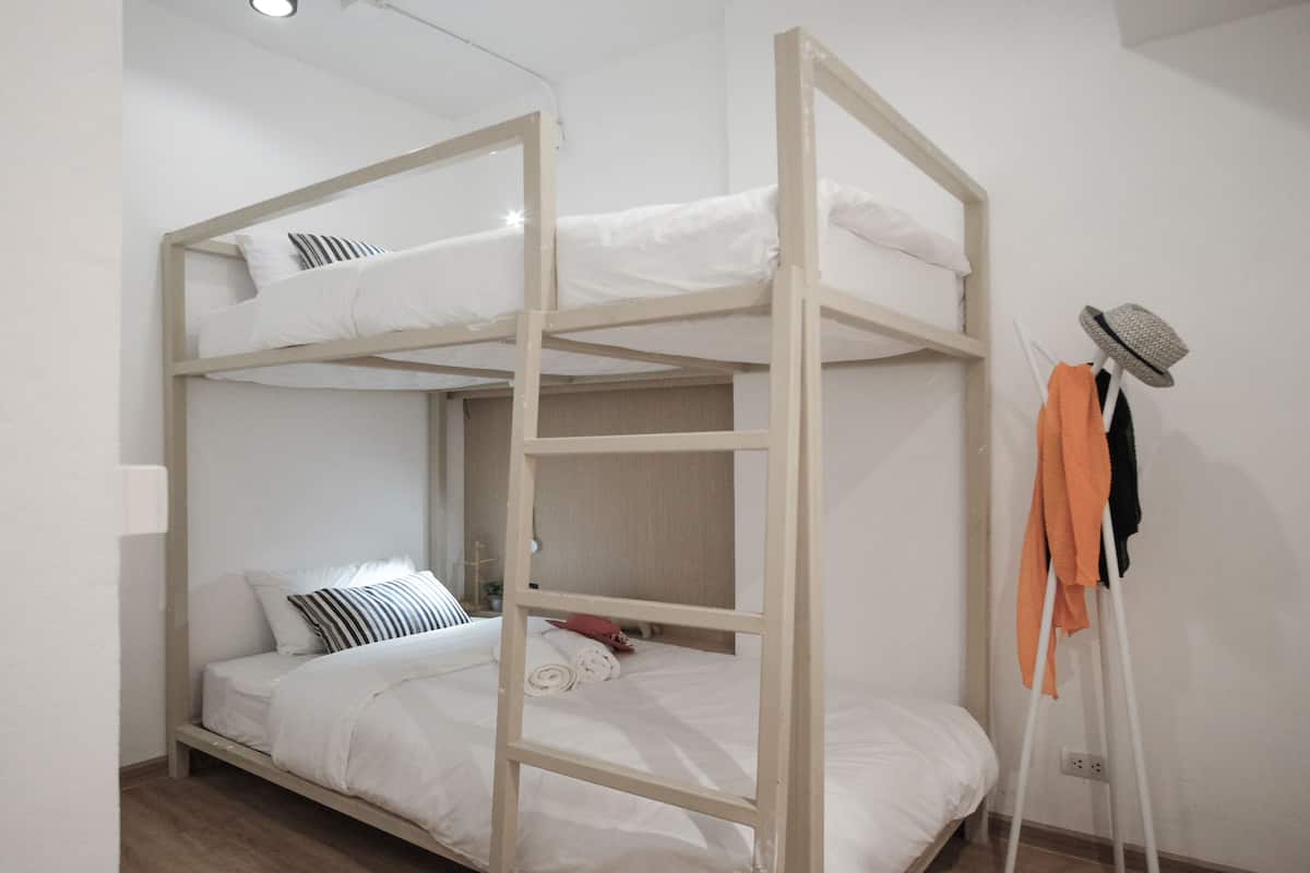 A bunk bed with white bedding, a wooden ladder, and a clothing rack with a hat.