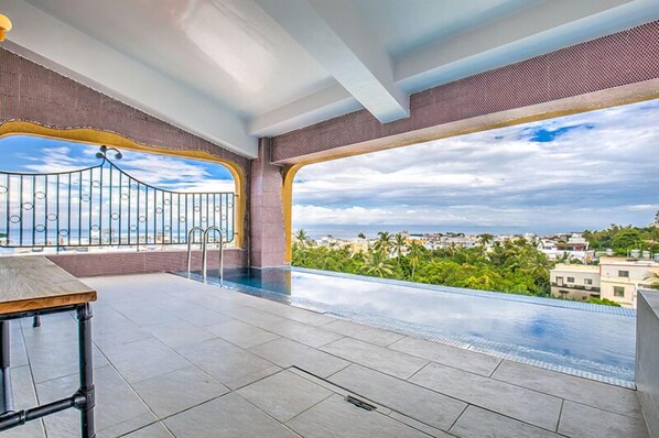 Piscina infinita no terraço com vista para o horizonte urbano e palmeiras.