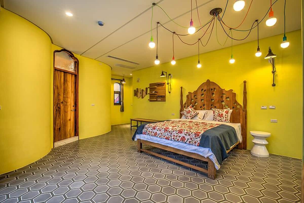 Une chambre à coucher avec un lit en bois, un mur jaune, un sol à motifs hexagonaux et une porte en bois.