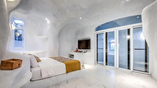 A modern bedroom with a curved ceiling, a bed with a wooden chest, a TV, and a sliding glass door leading to a balcony. - Wien Art Villa (Liuqiu)
