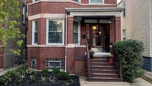 A two-story brick townhouse with a front porch, a small garden, and a visible number "2312" on the door. - Family-friendly, stylish Chicago Apartment in Logan Square (Chicago)