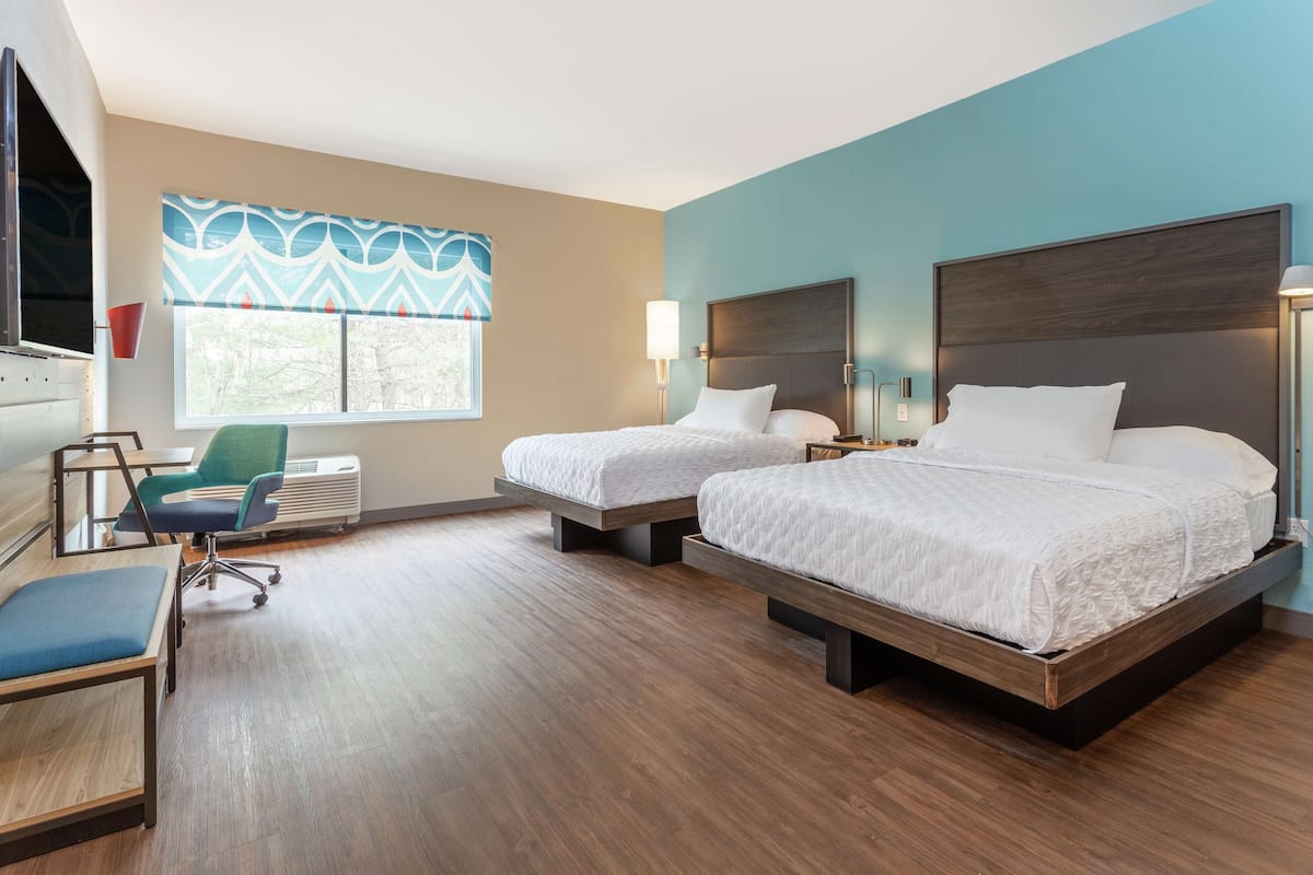 Habitación de hotel con dos camas, un escritorio, una silla y un ventanal con cortinas estampadas.