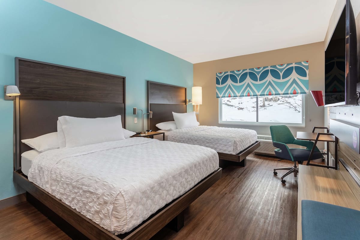 Una habitación de hotel con dos camas, un escritorio, una silla y un televisor.