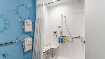 Un baño moderno con ducha, barras de apoyo, toallero y un pequeño banco.