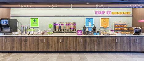 A breakfast counter with a variety of food and drink options, including yogurt, coffee, and donuts.