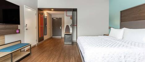 Une chambre d’hôtel moderne avec un grand lit, un banc, une télévision et une petite kitchenette.