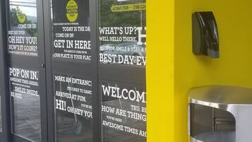 A building entrance with glass doors and yellow walls, featuring welcoming signs and a trash bin.