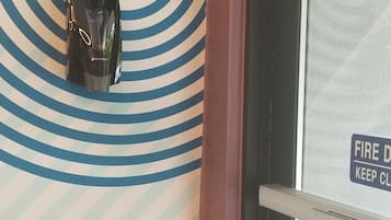 Una esquina de una habitación con un papel tapiz estampado, una puerta con un letrero de seguridad contra incendios y un objeto negro en la pared.