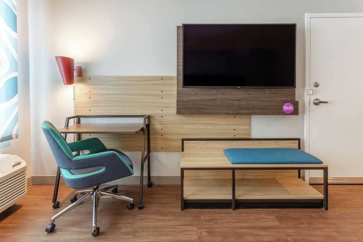 Una habitación de hotel con una cama, un escritorio, una silla, un televisor y una puerta.