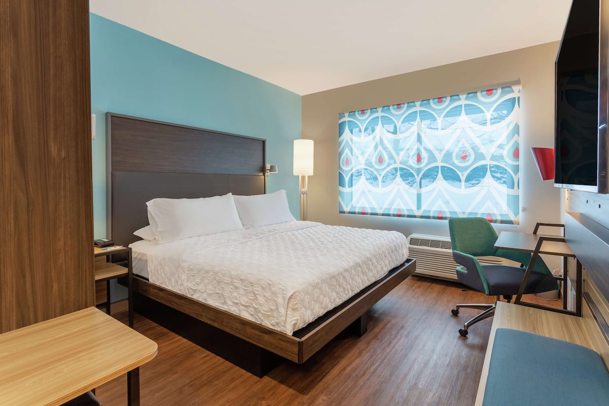 Una habitación de hotel moderna con cama, escritorio, silla y un gran ventanal con cortinas estampadas.