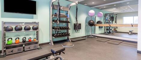Un gimnasio con equipamiento de ejercicio, una televisión y un espejo.