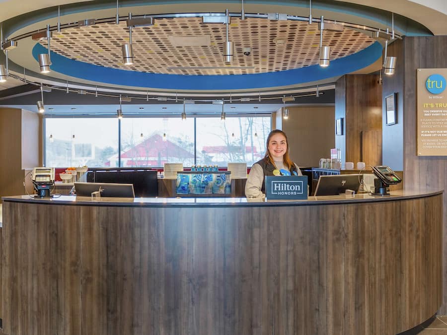 A hotel reception desk with a modern design, a large window, and a sign indicating Hilton Honors membership.