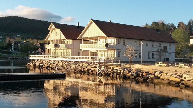 A waterfront building with a balcony, a dock, and a rocky shoreline.
