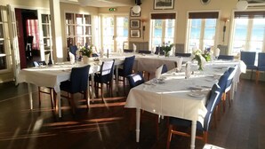 A dining area with tables set for service, large windows with ocean views, and a staircase leading to an upper level.