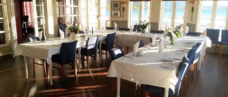 A dining area with tables set for service, large windows with ocean views, and a staircase leading to an upper level.