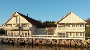 A two-story wooden building with balconies, a stone foundation, and a white fence.