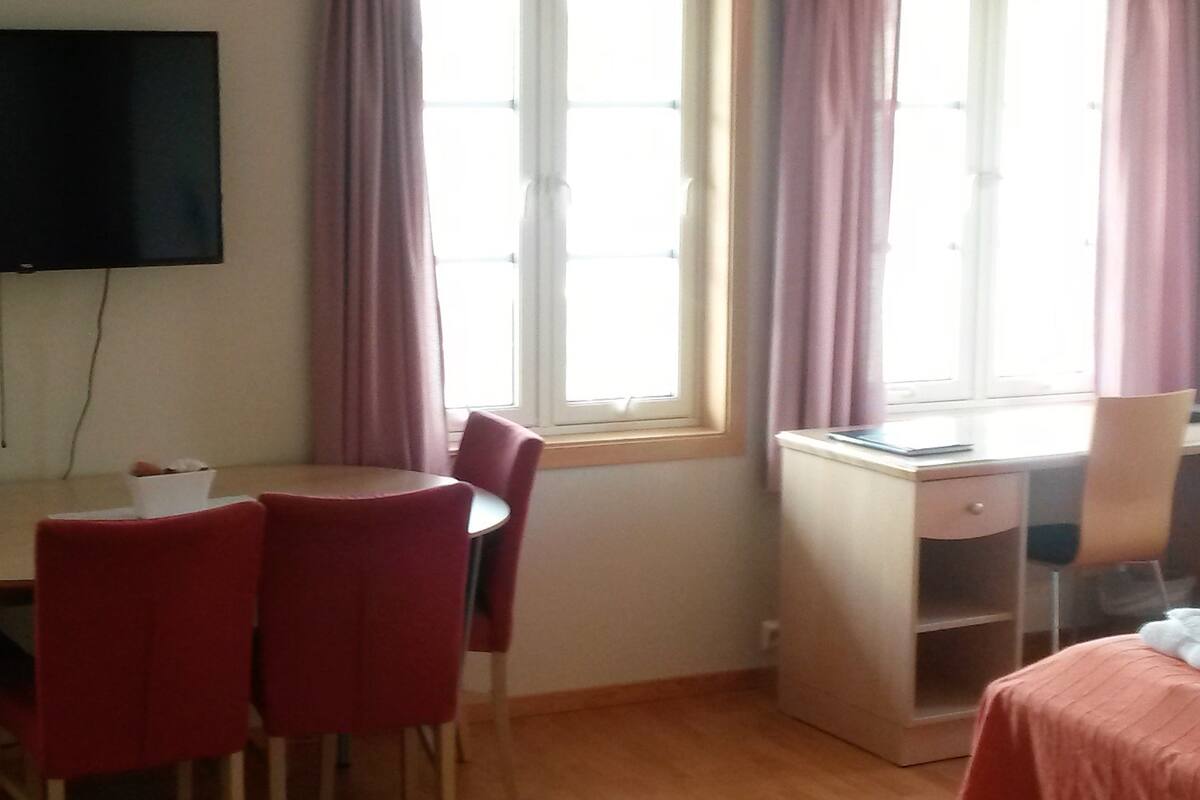 Een kamer met een bed, een bureau, een stoel, een televisie en een raam met gordijnen.