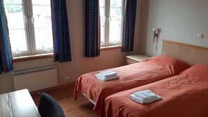 A hotel room with two beds, a desk, and a window with curtains.