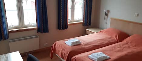 A hotel room with two beds, a desk, and a window with curtains.
