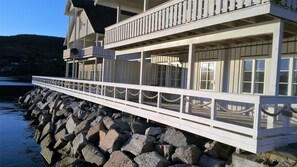 A waterfront building with a balcony, large windows, and a stone foundation.