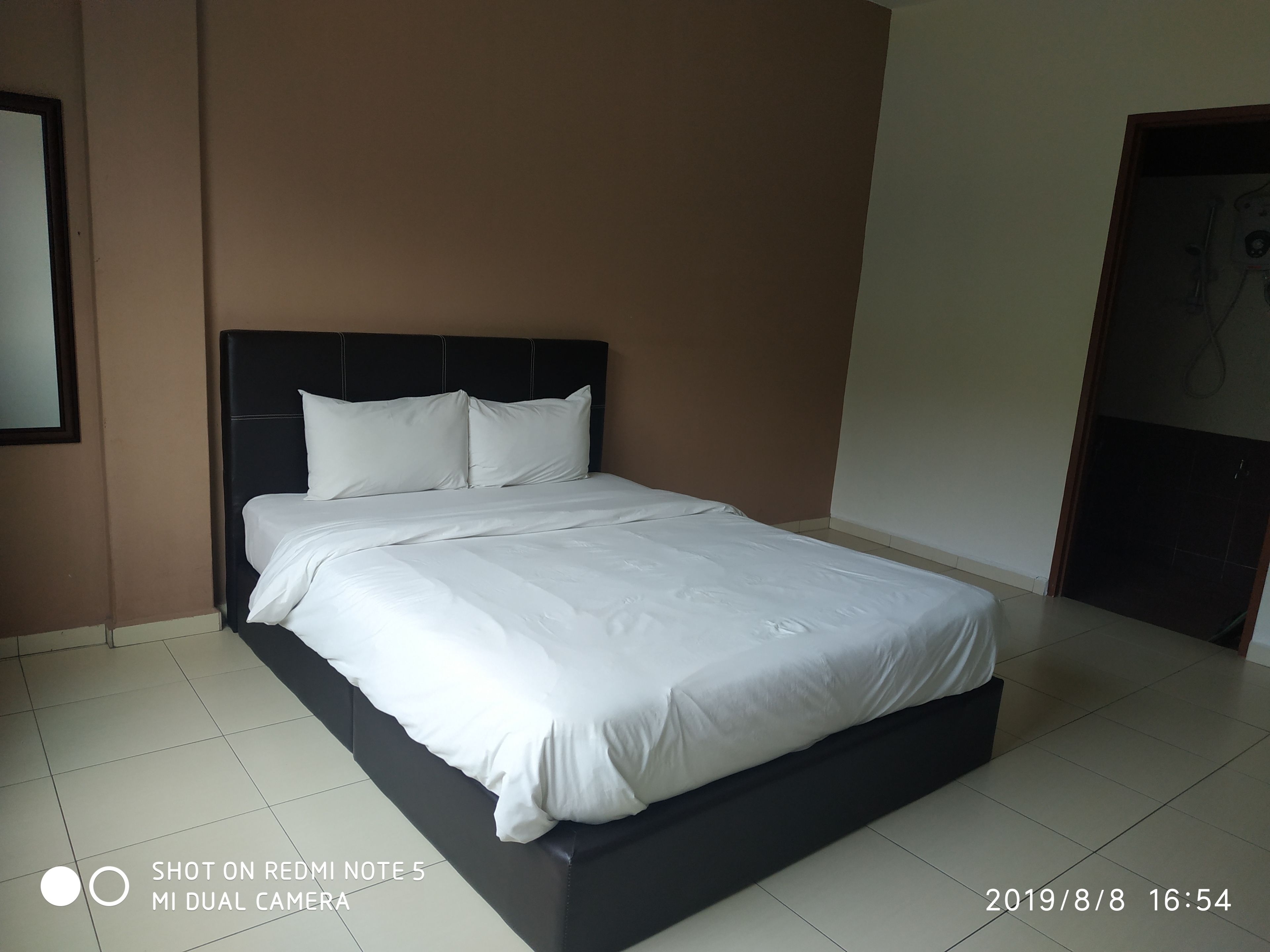 A neatly made bed in a hotel room with a dark headboard and white bedding.