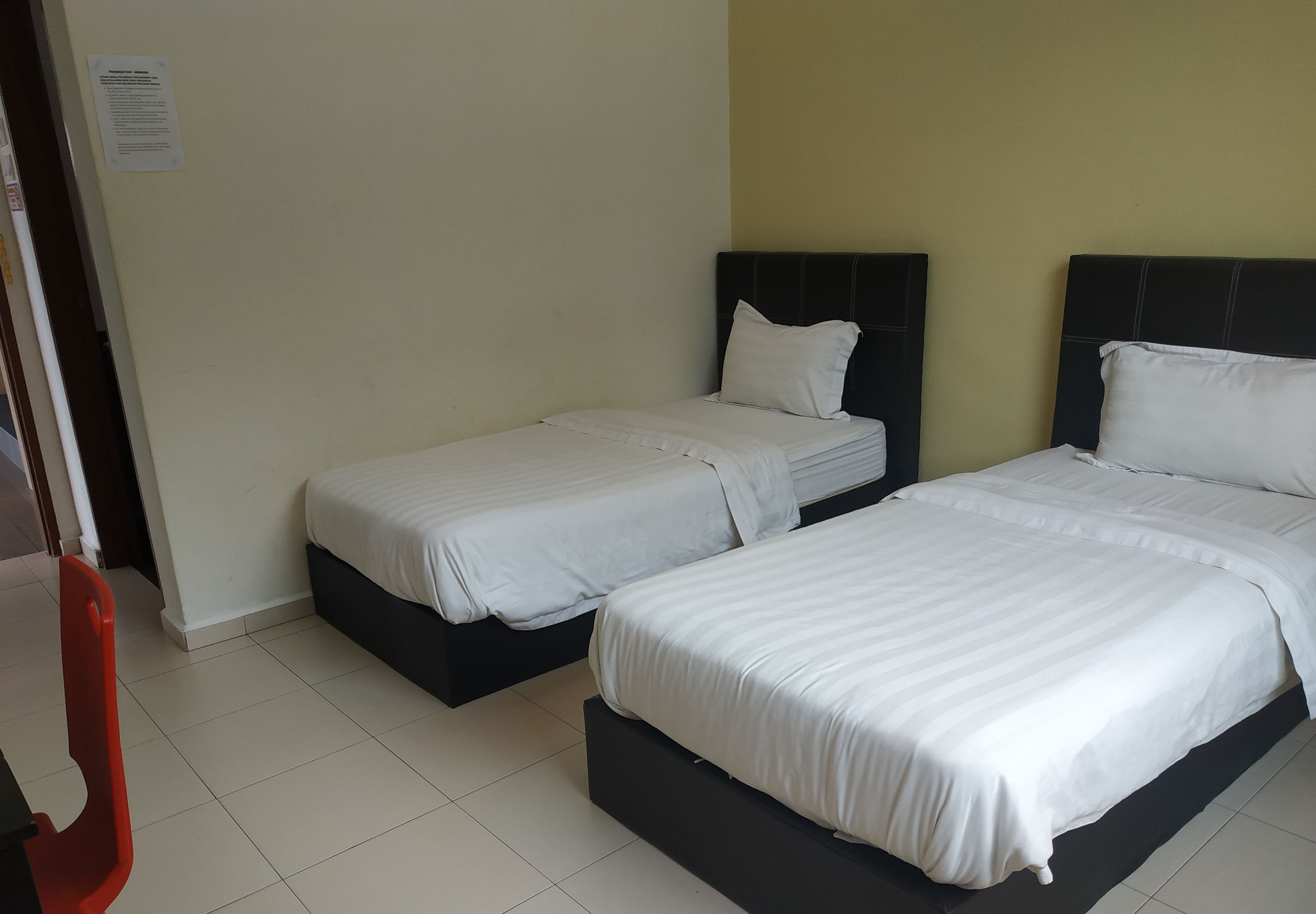 A hotel room with two single beds, a red chair, and a white door.