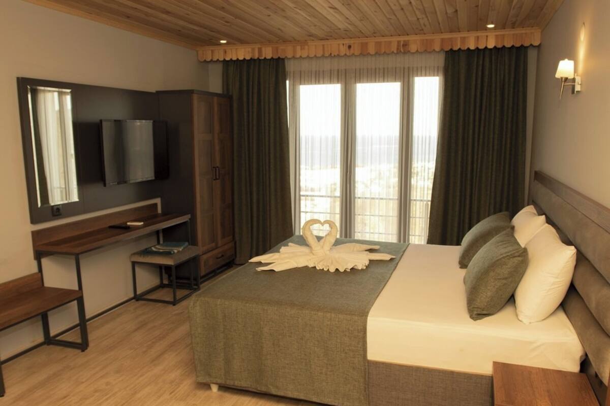 A hotel room with a bed, a TV, a desk, and a window with curtains.