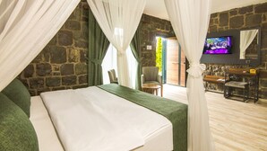 Un dormitorio con una cama grande, televisor, pared de piedra y una silla verde.
