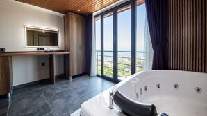 Un baño moderno con una bañera grande, un tocador con espejo y vistas a la ciudad a través de amplias ventanas.