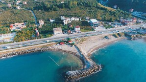 Vista aérea de un pueblo costero con un rompeolas curvo destacado, una carretera principal y edificios residenciales.