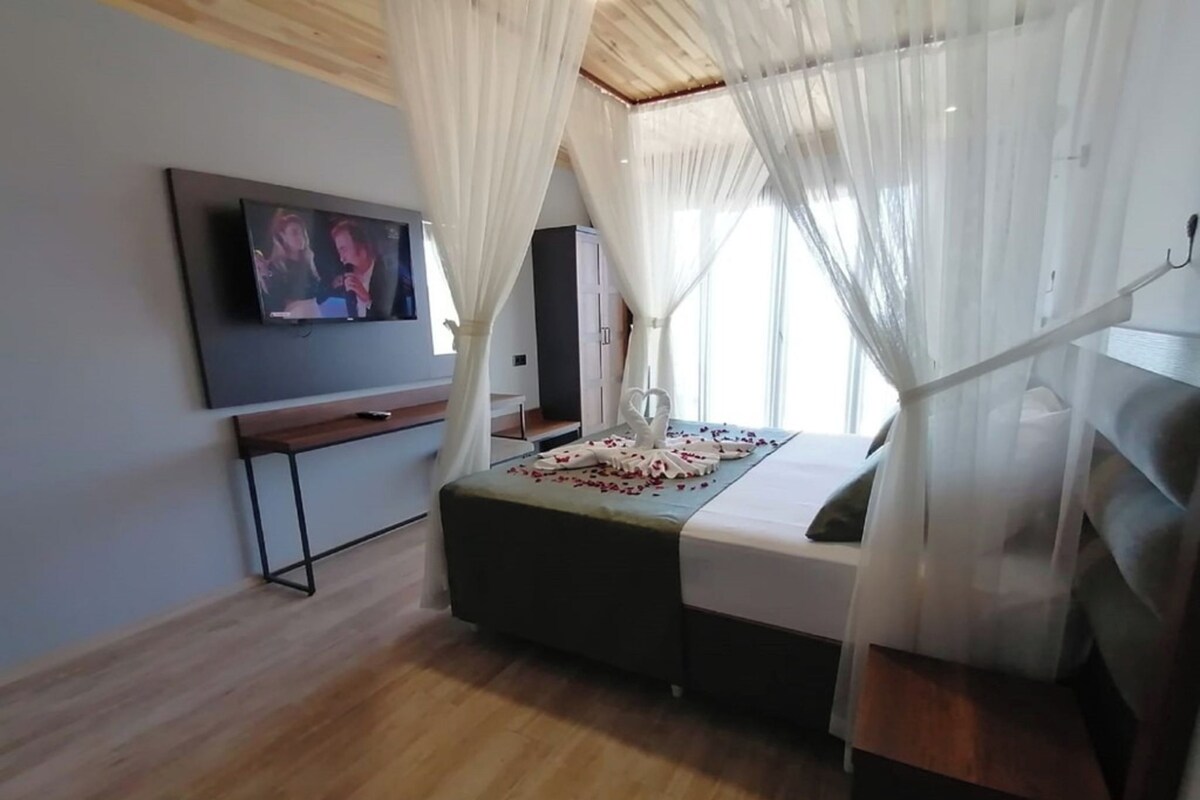Un dormitorio con cama, televisión y ventana con cortinas translúcidas.