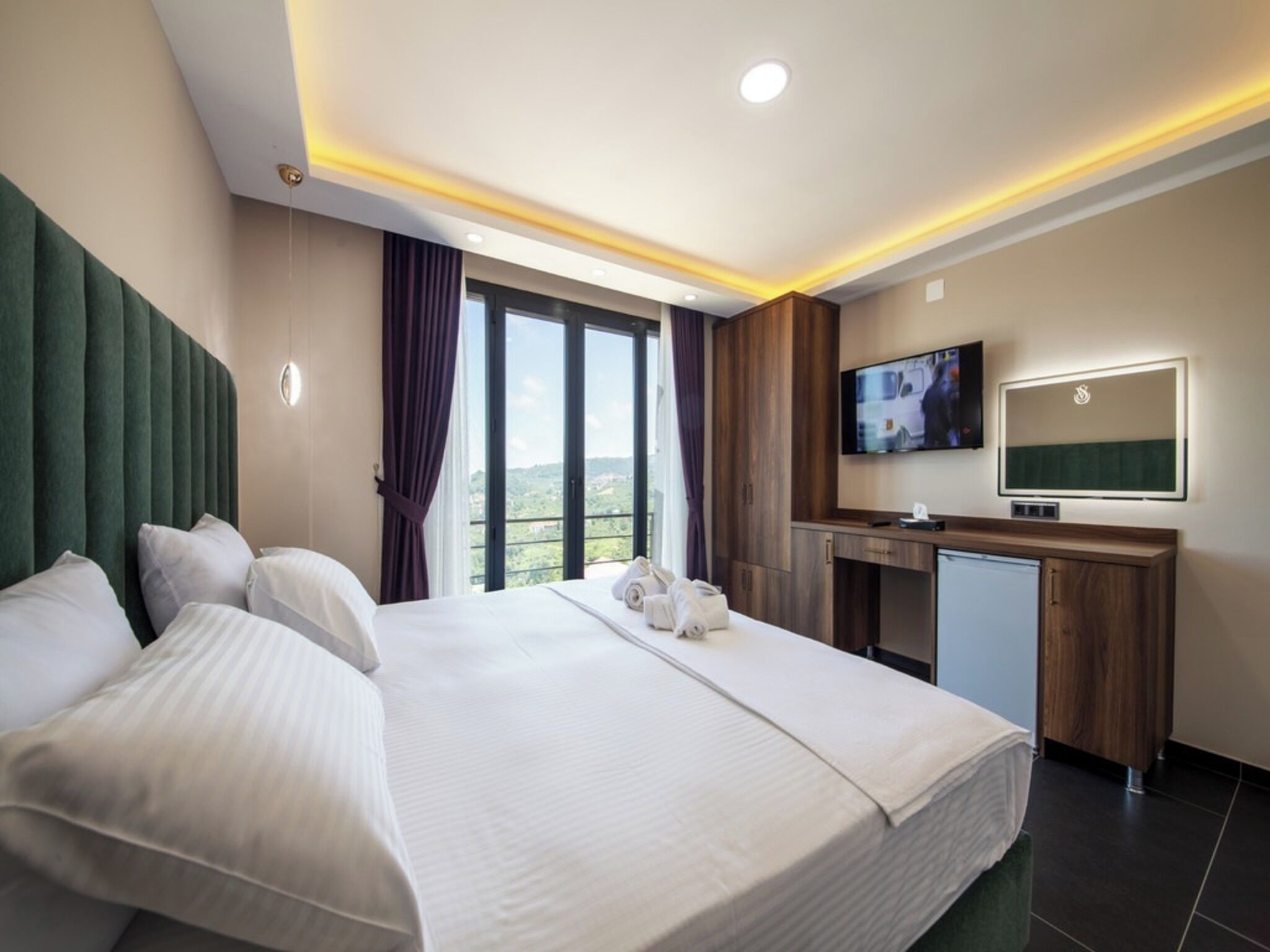 Ein Hotelzimmer mit einem großen Bett, einem Schreibtisch, einem Fernseher und Blick ins Freie.