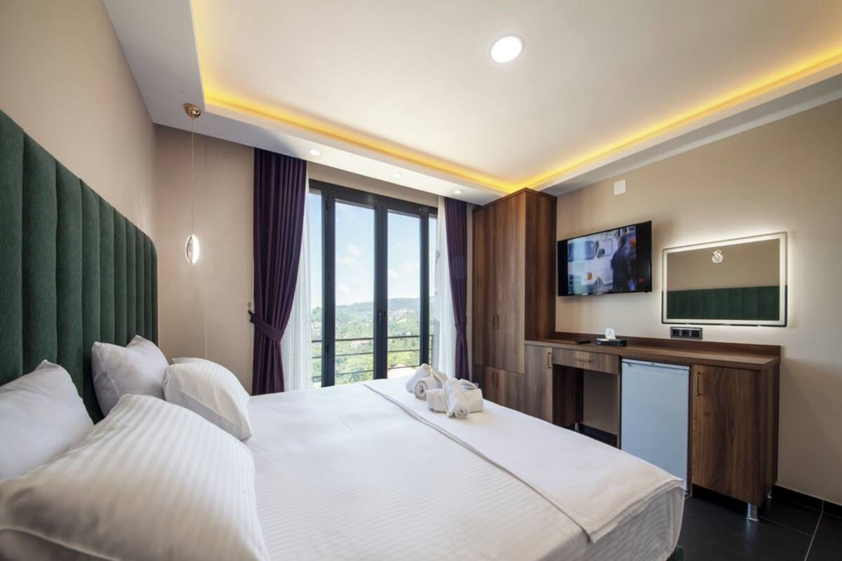 A hotel room with a large bed, a desk, a television, and a view of the outdoors.