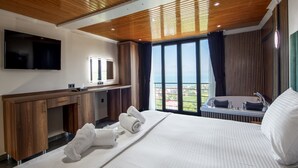 Una habitación de hotel moderna con techo de madera, una cama grande, televisión, escritorio y vistas al mar.
