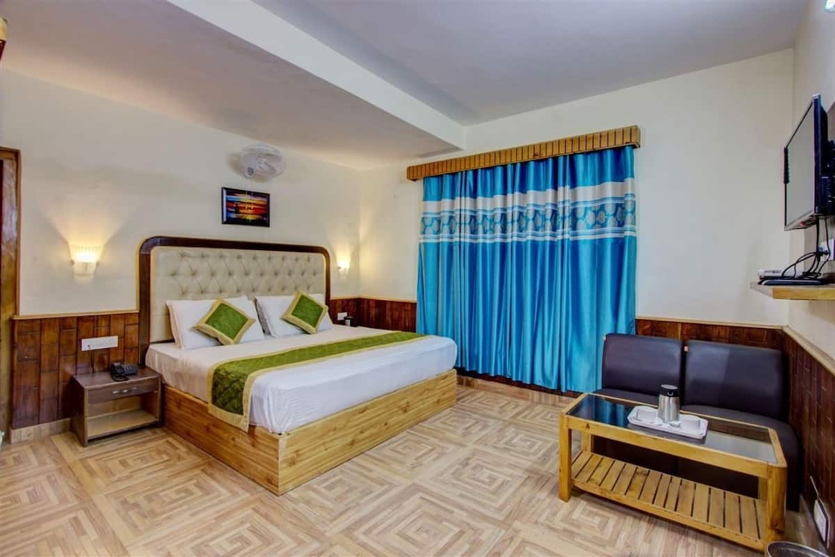 Una habitación de hotel con una cama grande, una mesita de noche de madera, una pequeña mesa con una bandeja, un sofá y un televisor montado en la pared.