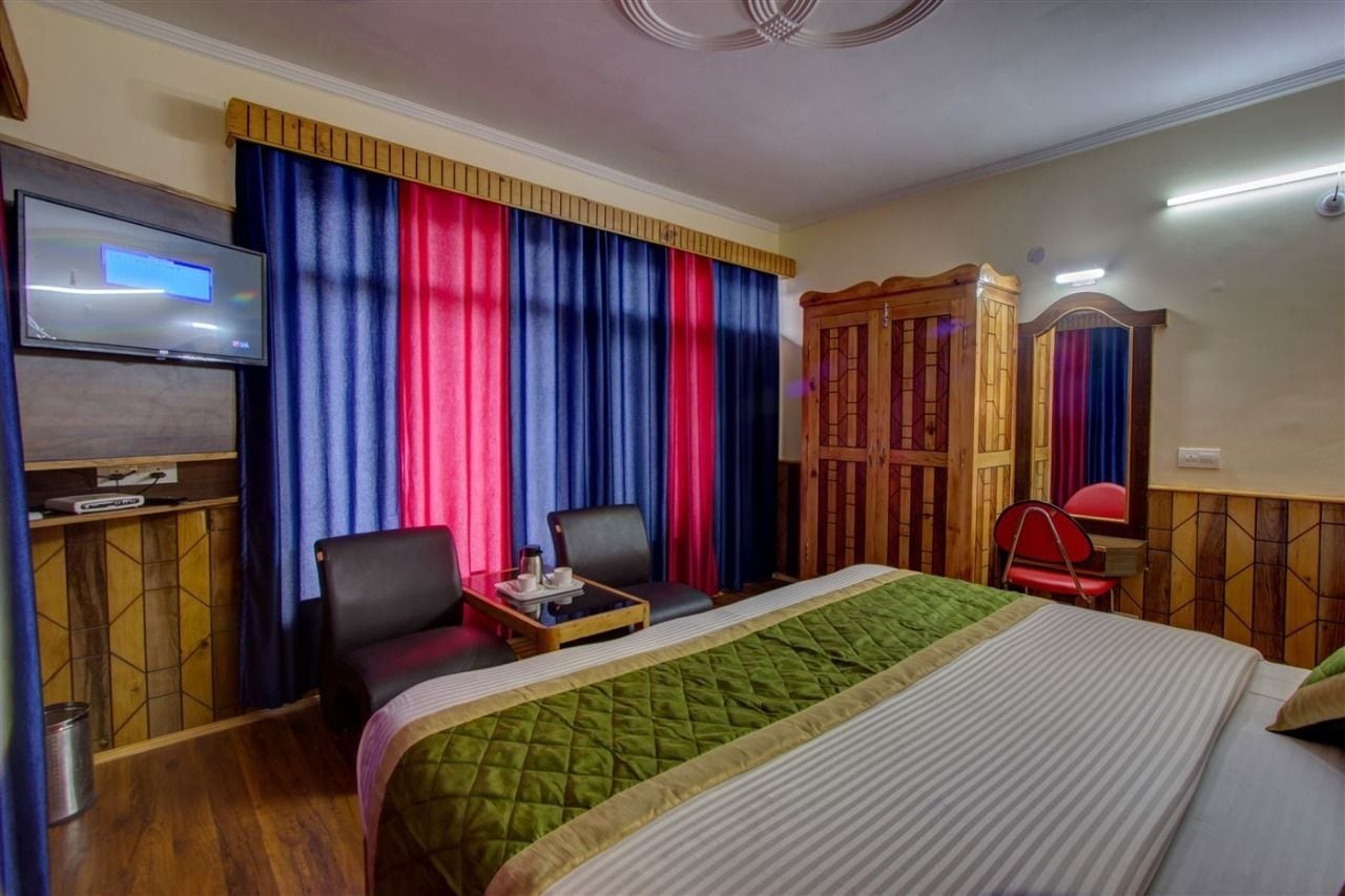 A hotel room with a bed, a TV, a desk with a chair, and a wardrobe.