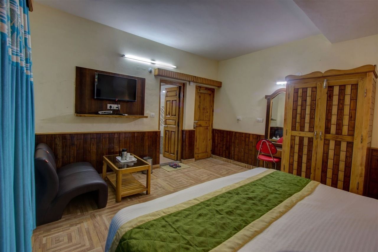 A hotel room with a bed, a TV mounted on the wall, a wooden wardrobe, and a small table with a chair.