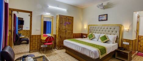 A hotel room with a bed, a small table with a cup and a thermos, a chair, a mirror, a wardrobe, and a ceiling fan.