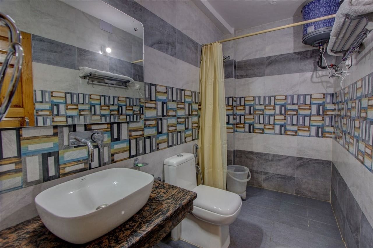 Een badkamer met een wit wastafel, toilet en douche. De muren zijn betegeld met een geometrisch patroon.