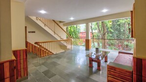 A spacious indoor area with a staircase leading to a balcony. The balcony overlooks a lush green garden. - Hotel Samiru (Manali)
