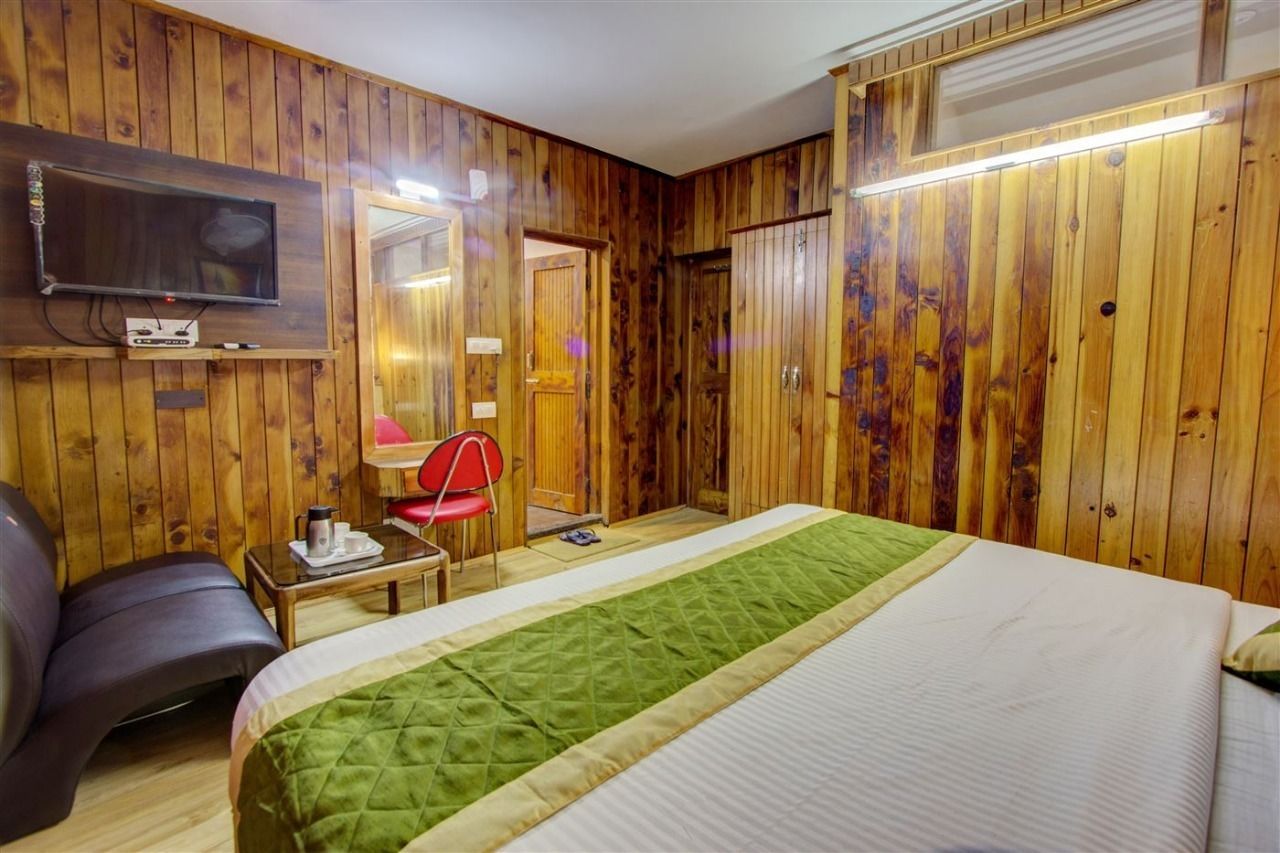 Une pièce aux murs recouverts de lambris en bois, un lit avec une literie verte et blanche, une chaise rouge, un bureau avec une lampe et un téléviseur fixé au mur.