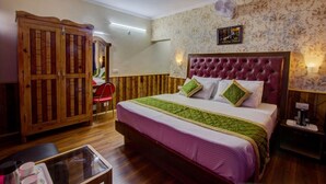 A hotel room with a large bed, a wooden wardrobe, a red chair, and a small table with cups and a tray. - Hotel Samiru (Manali)
