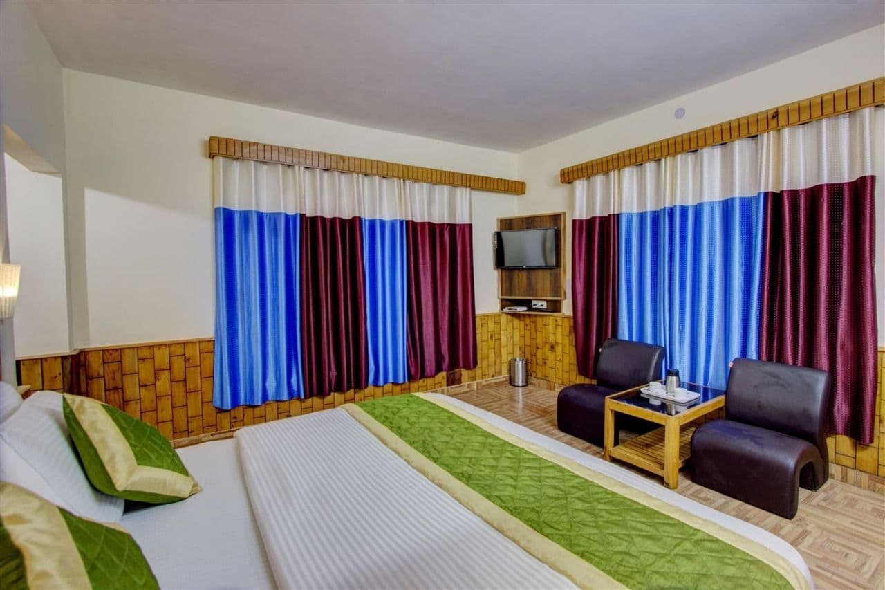 A hotel room with a bed, two chairs, a small table, a TV, and curtains with a striped pattern.