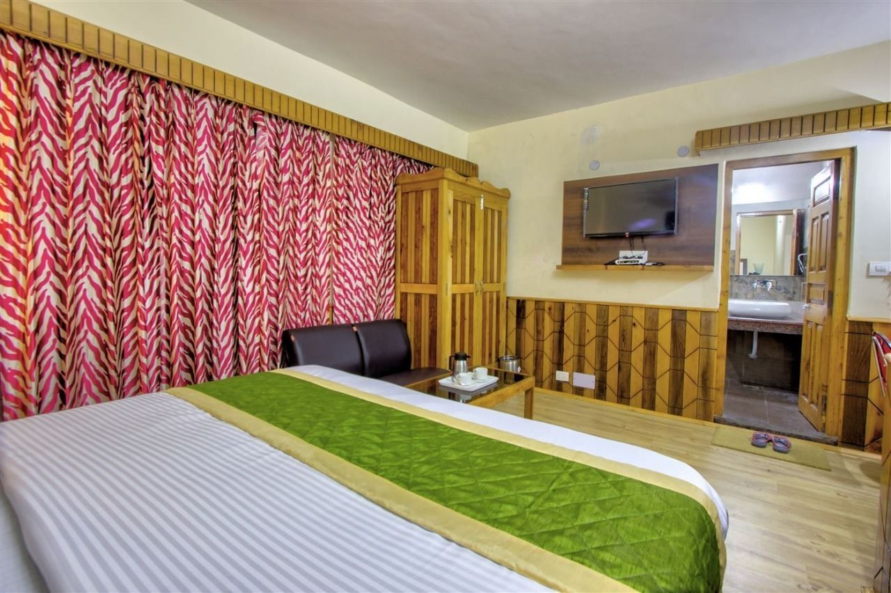 Ein Hotelzimmer mit einem Bett, einem Fernseher, einem Holzschrank und einem durchgegangene Tür sichtbaren Badezimmer.