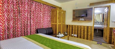 A hotel room with a bed, a TV, a wooden cabinet, and a bathroom visible through an open door.